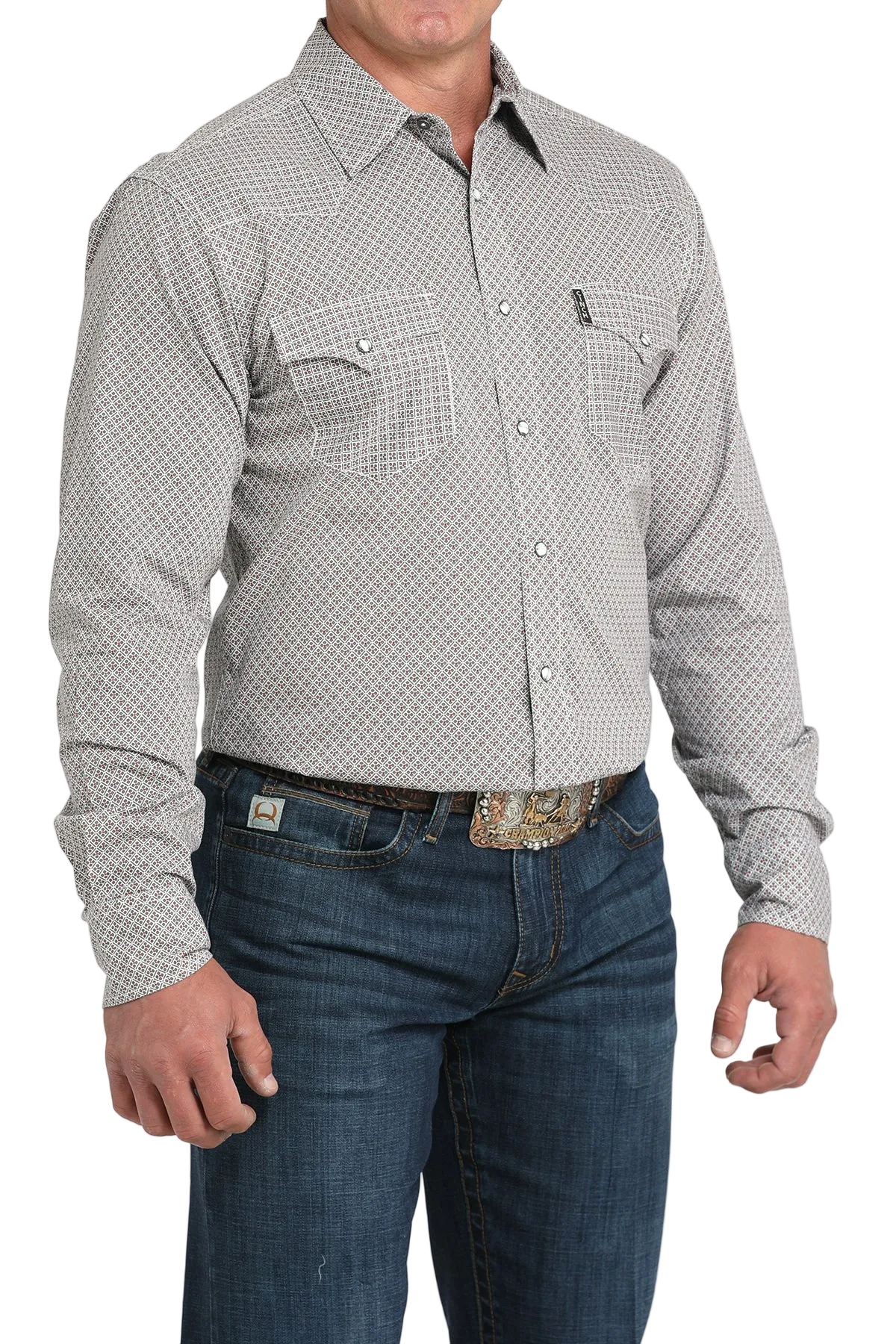 A man wearing a light gray patterned button-up shirt, dark jeans, and a large belt buckle, standing against a transparent background