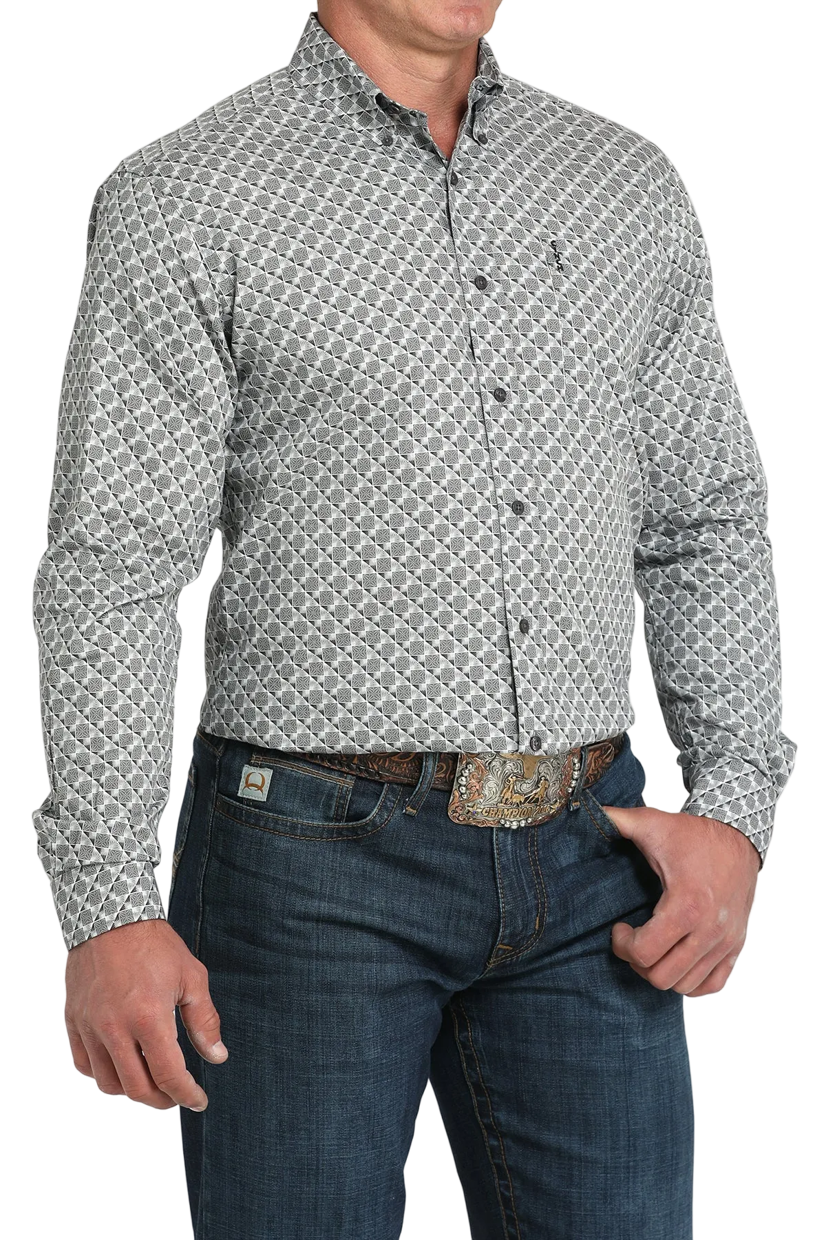 A man wearing a light gray patterned button-up shirt, dark jeans, and a large belt buckle, standing against a white background