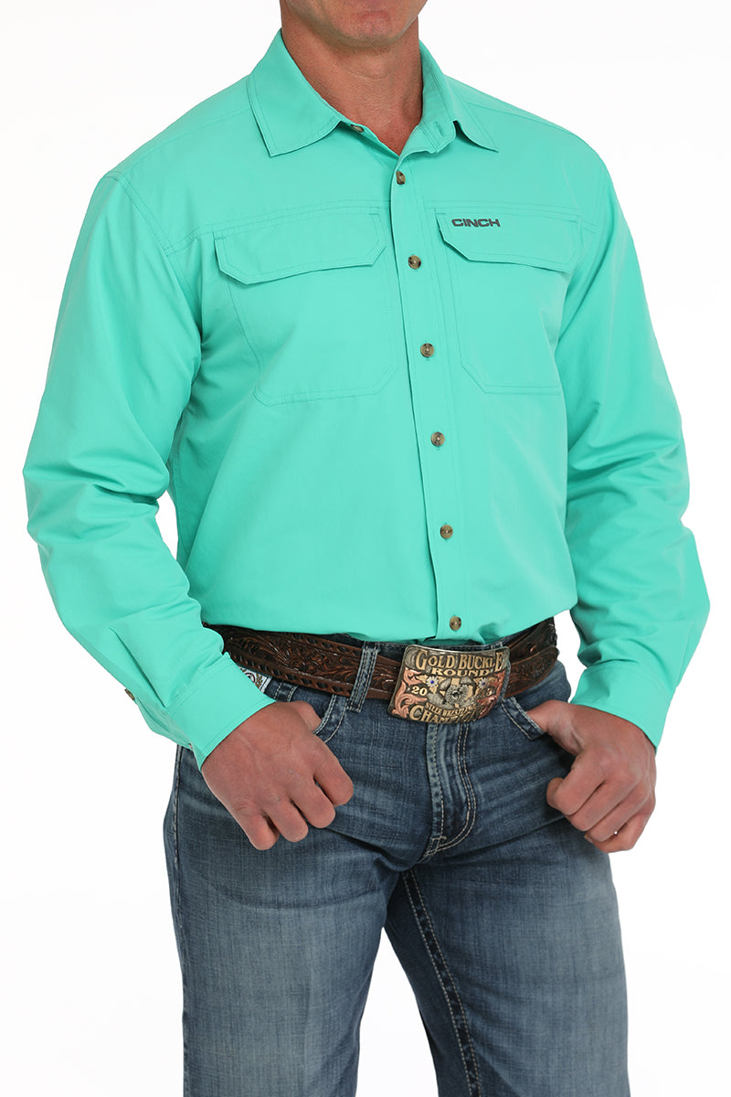 Person wearing a light green shirt with a brand logo, paired with blue jeans on a white background
