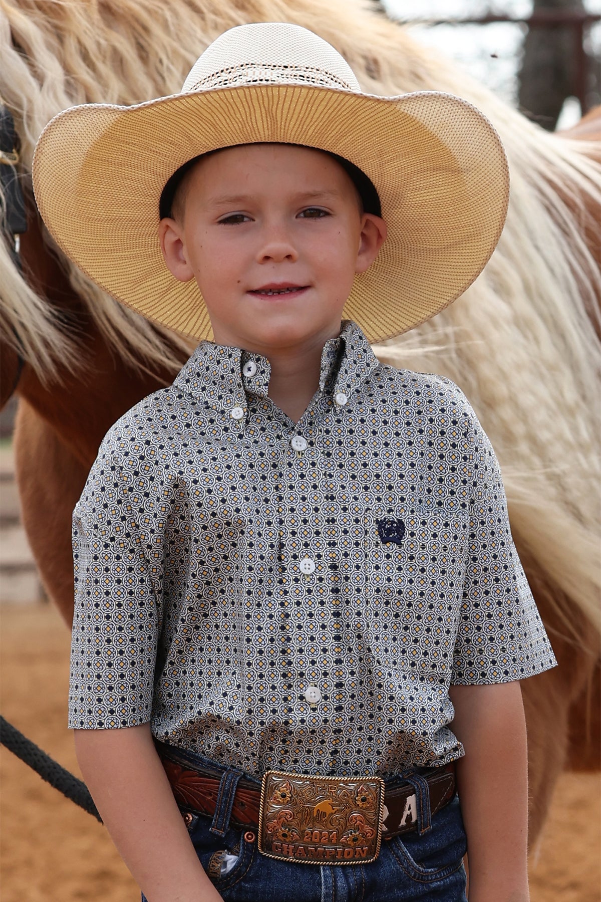 Young boy wearing a straw hat and patterned CINCH shirt standing next to a horse.
