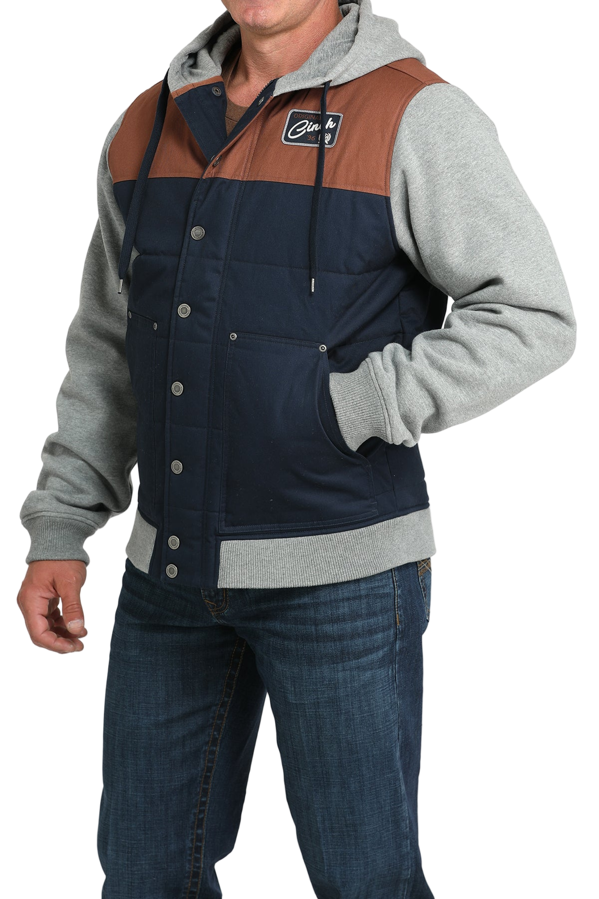 Man wearing a navy and brown snap-front jacket with light gray sleeves and a hood, paired with blue jeans