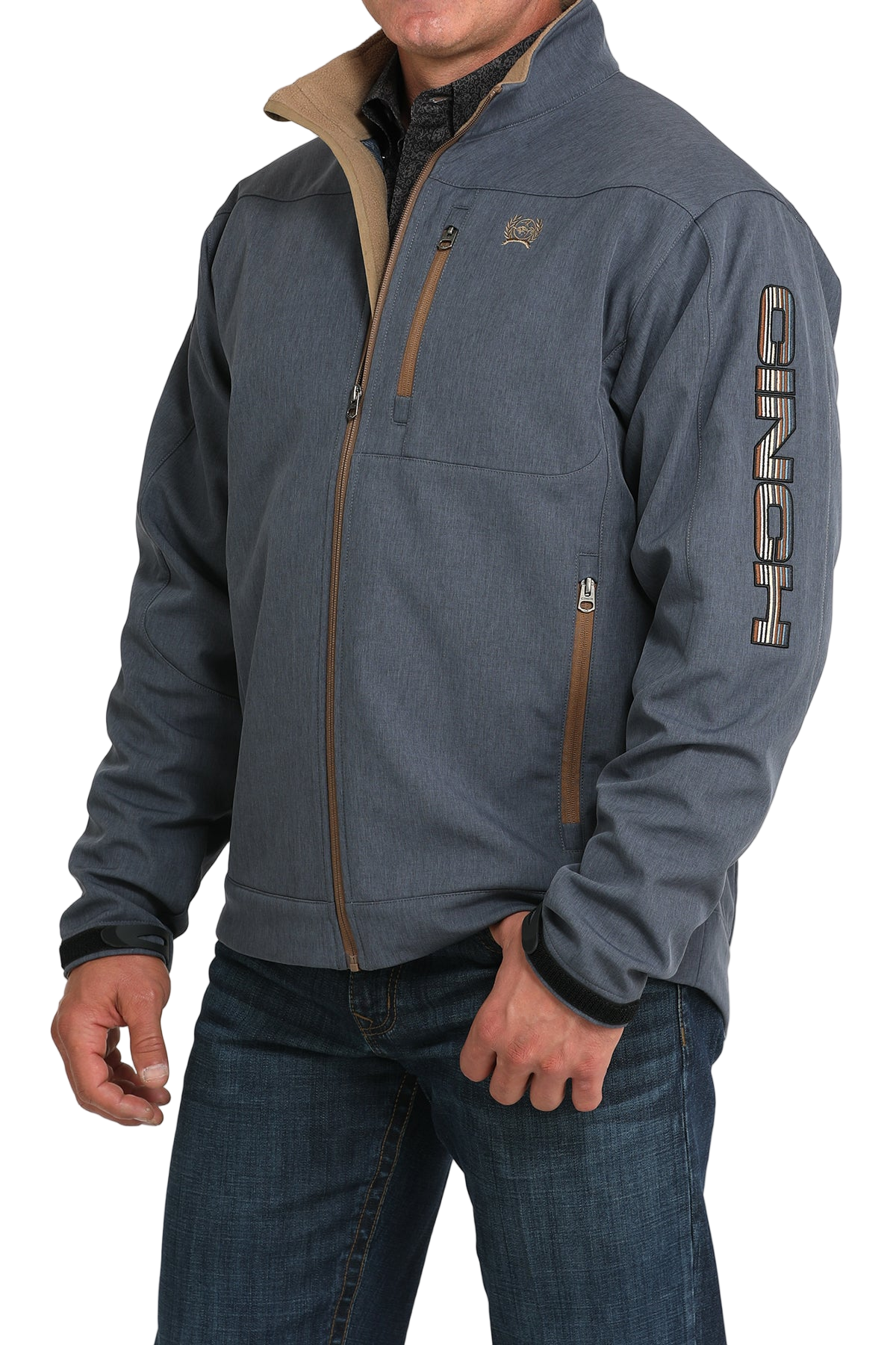 Man wearing a blue softshell jacket with tan trim and “CINCH” lettering down the sleeve, paired with blue jeans