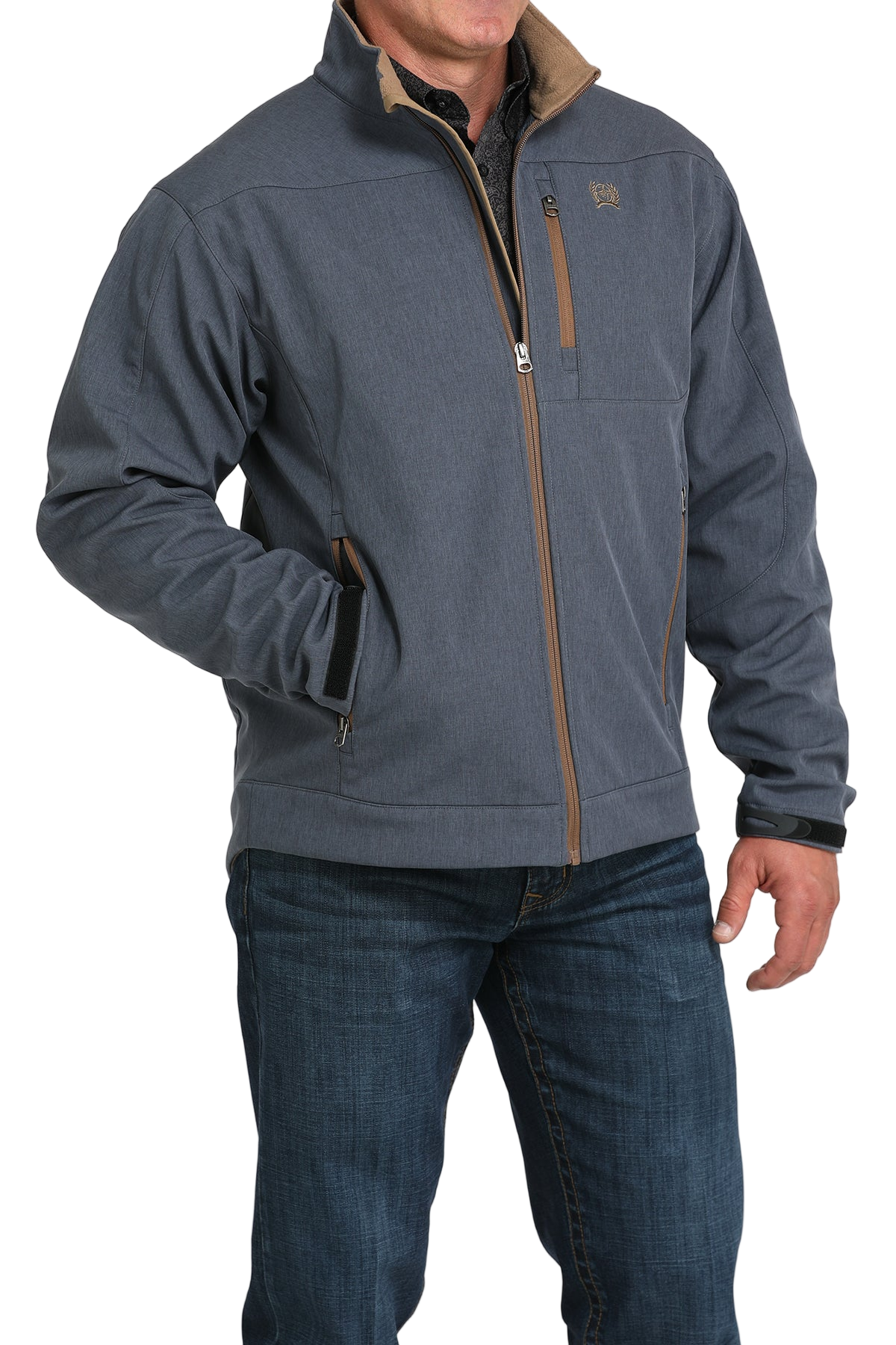 Man wearing a blue softshell jacket with tan trim, paired with blue jeans