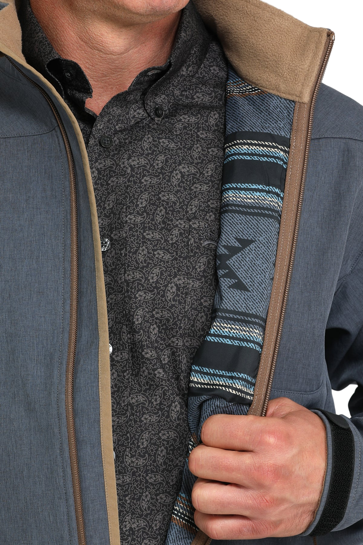 Man wearing a blue softshell jacket, holding it open to show the patterned interior lining with blue and black southwestern-style stripes