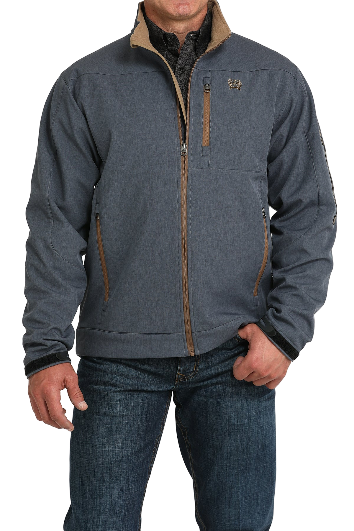 Man wearing a blue softshell jacket with tan trim, paired with blue jeans