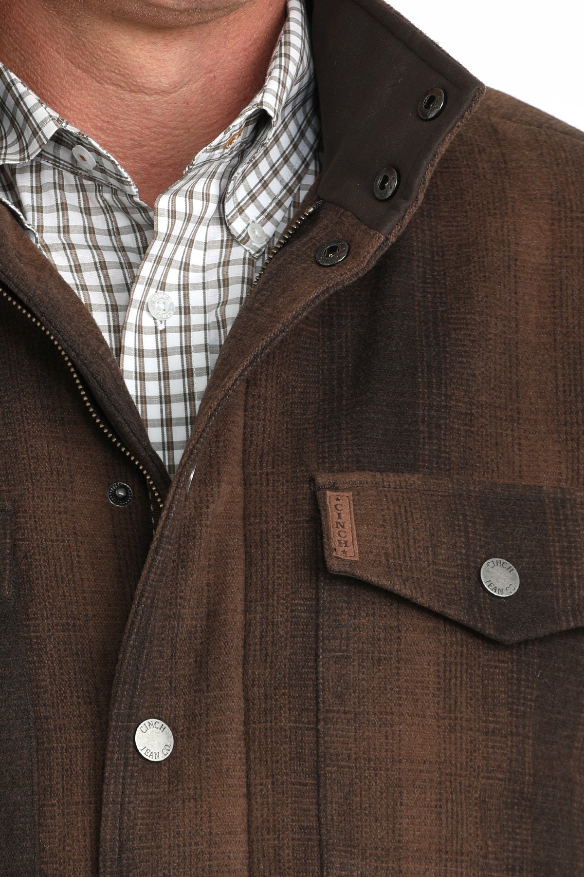 Close-up of a man wearing a brown plaid jacket with buttons and pockets and an undershirt 