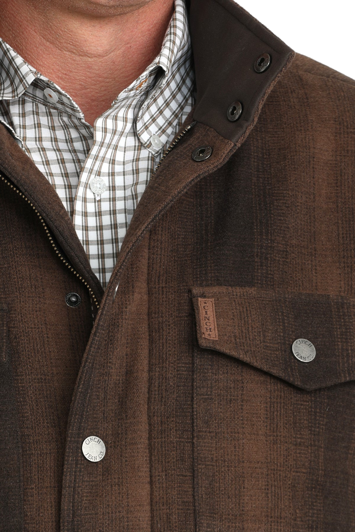 Close-up of a man wearing a brown button-front jacket with multiple flap pockets and a patterned shirt underneath