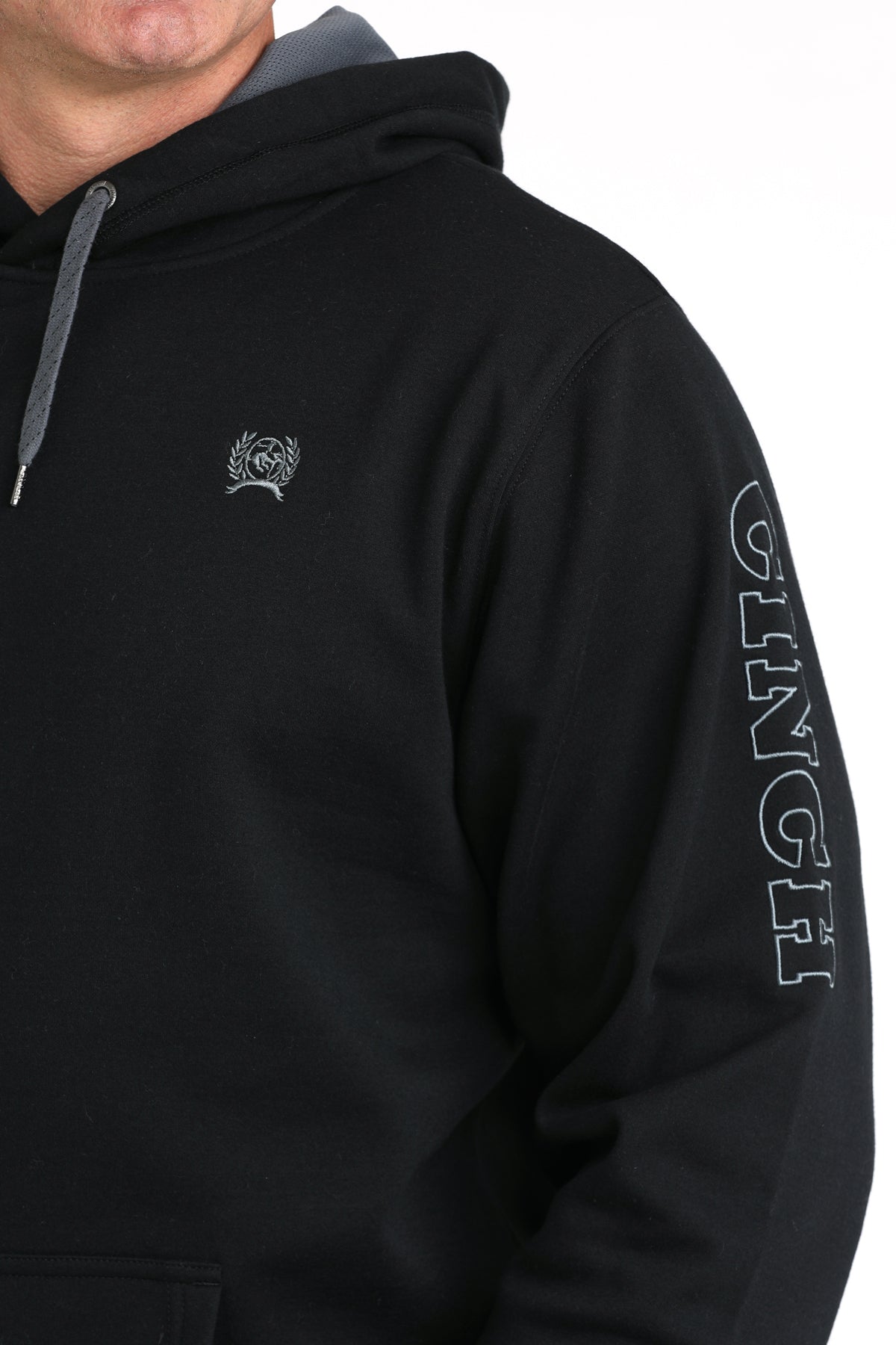 Black hoodie with a logo on the chest and text on the sleeve, worn by a person.
