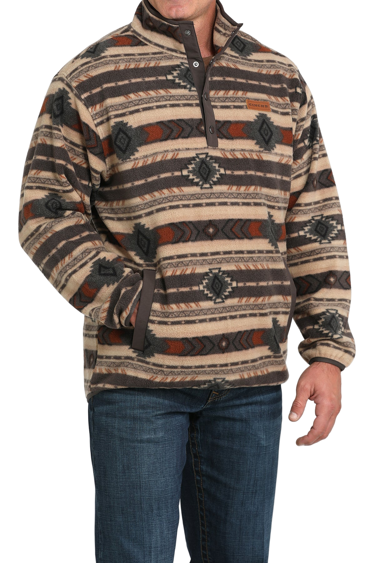 Man wearing a tan and brown patterned pullover with a buttoned placket and side pockets, paired with blue jeans