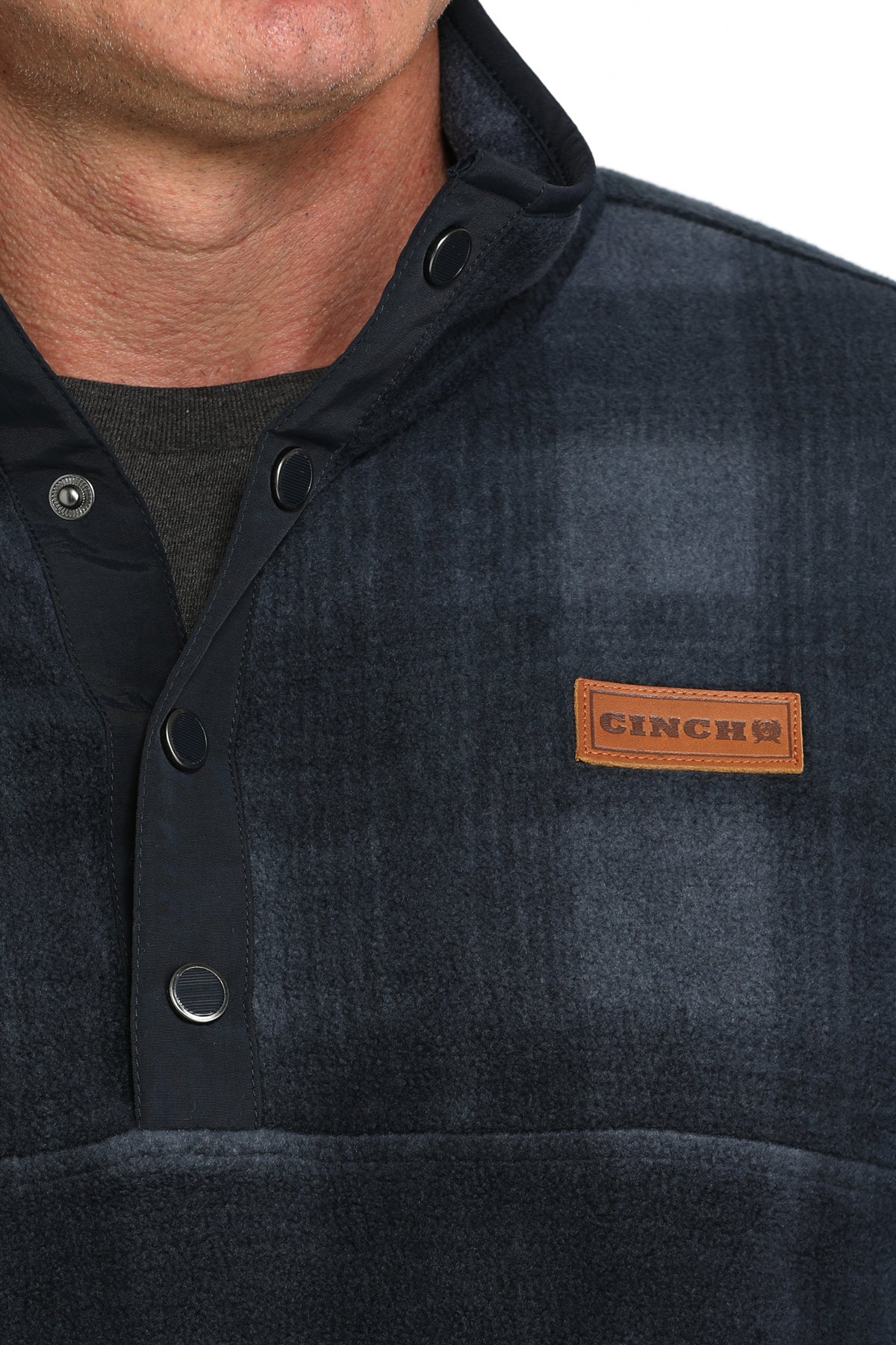 Close-up of a man wearing a blue checkered fleece pullover with buttons and a 'CINCH' logo