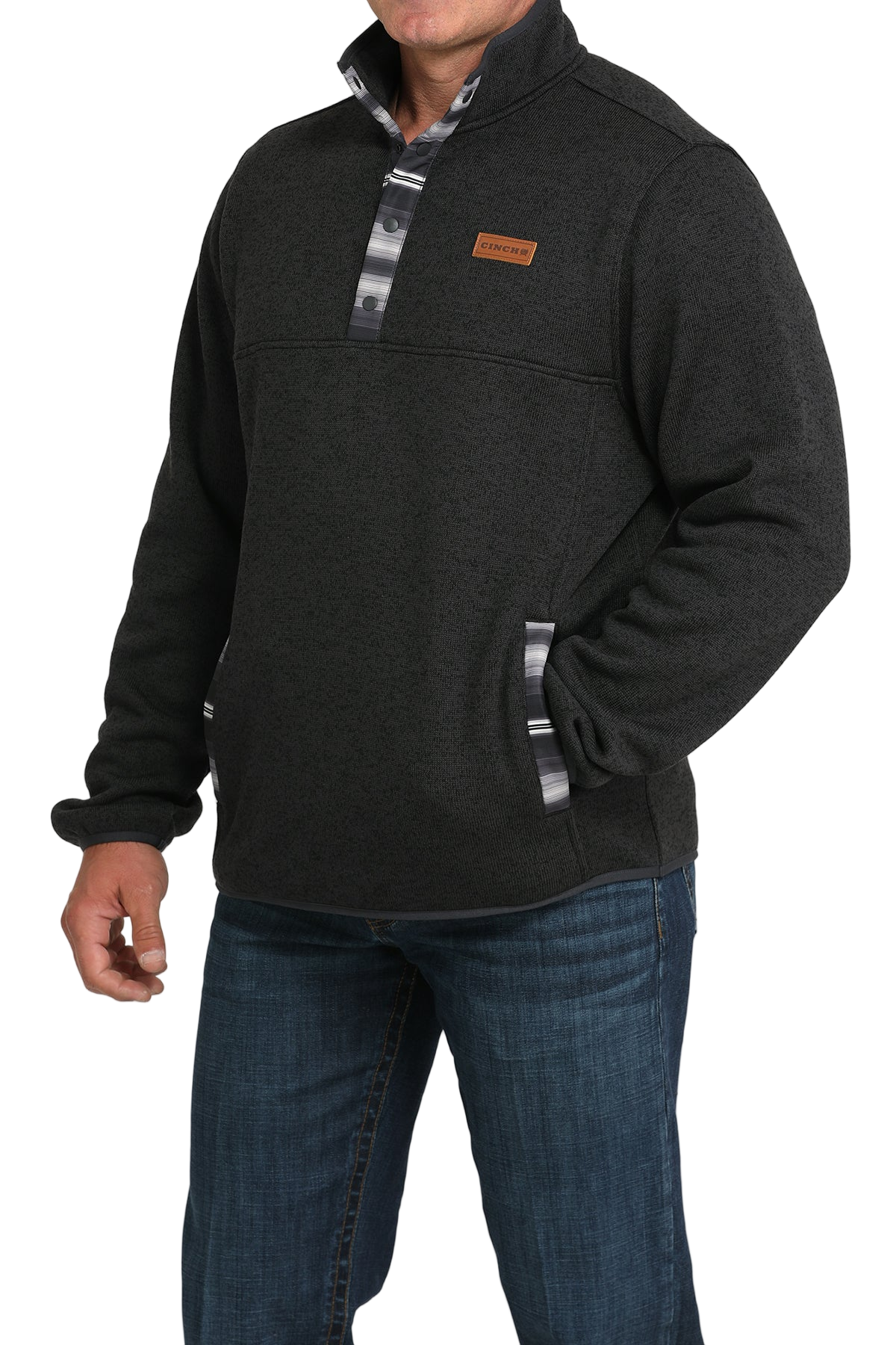 Man wearing a dark textured pullover with patterned trim on the placket and pockets, paired with blue jeans