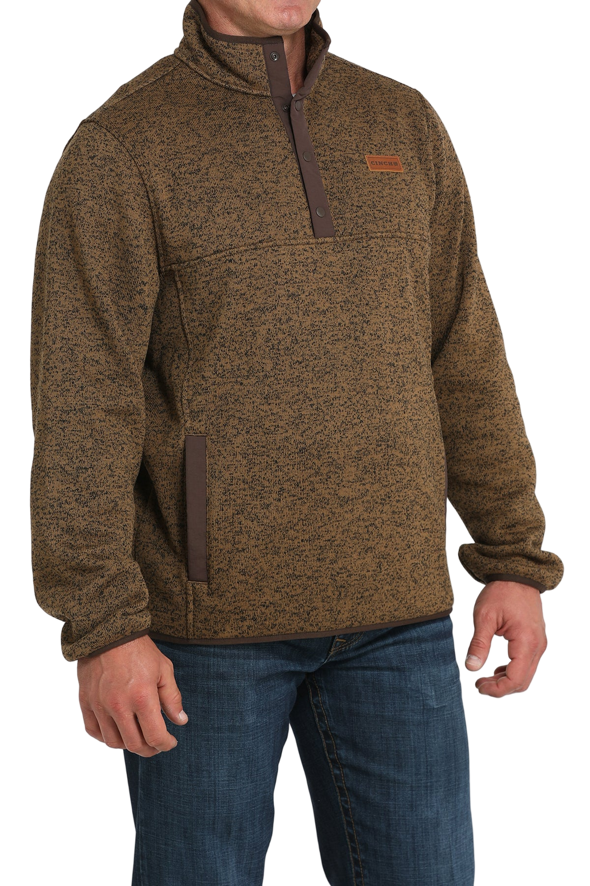 Man wearing a brown textured pullover with a snap-button placket, stand-up collar, and front hand pockets, paired with blue jeans