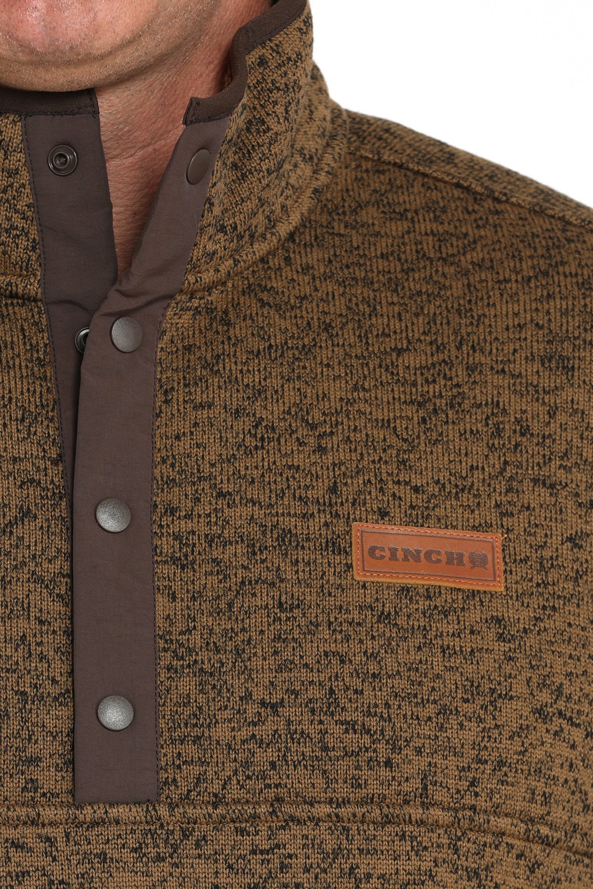 Close-up of a man wearing a khaki pullover jacket with buttons and a 'CINCH' logo