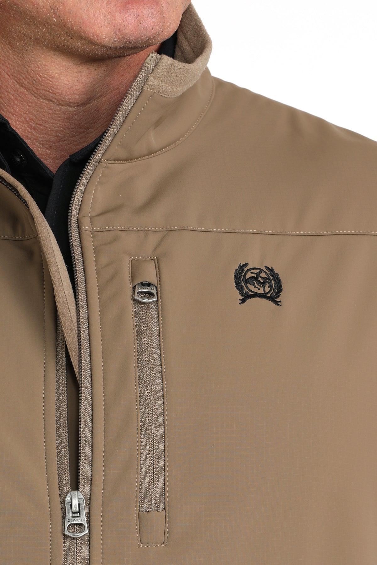 Close-up of a man wearing a khaki vest with a cinch logo