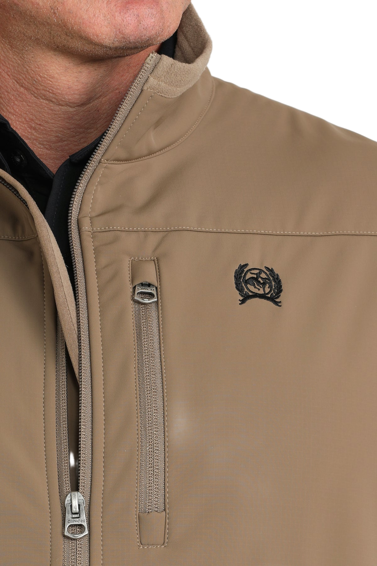 Close-up of a man wearing a tan zip-up vest with a chest pocket