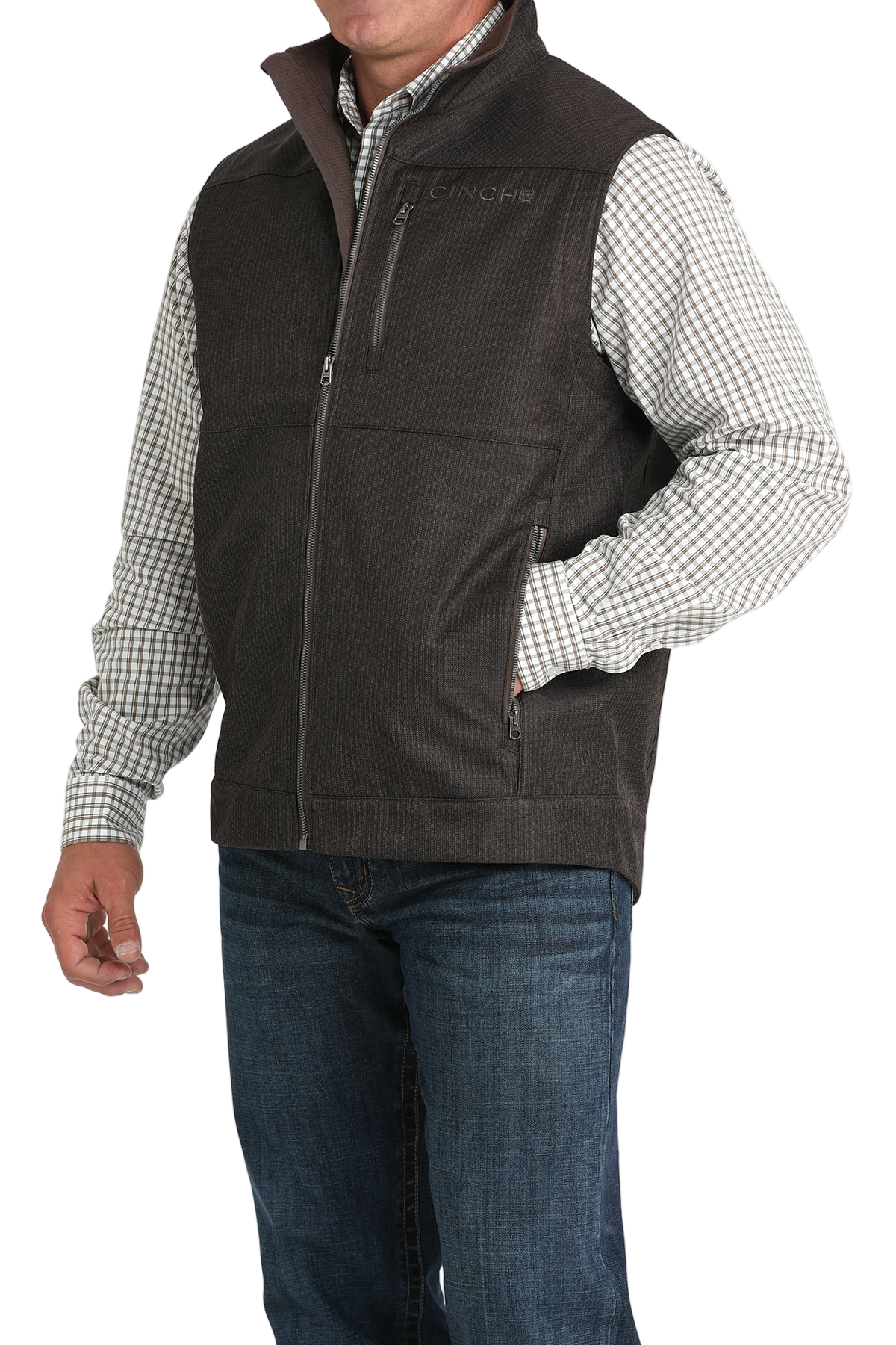 Man wearing a dark brown textured vest over a checked long-sleeve shirt, paired with blue jeans