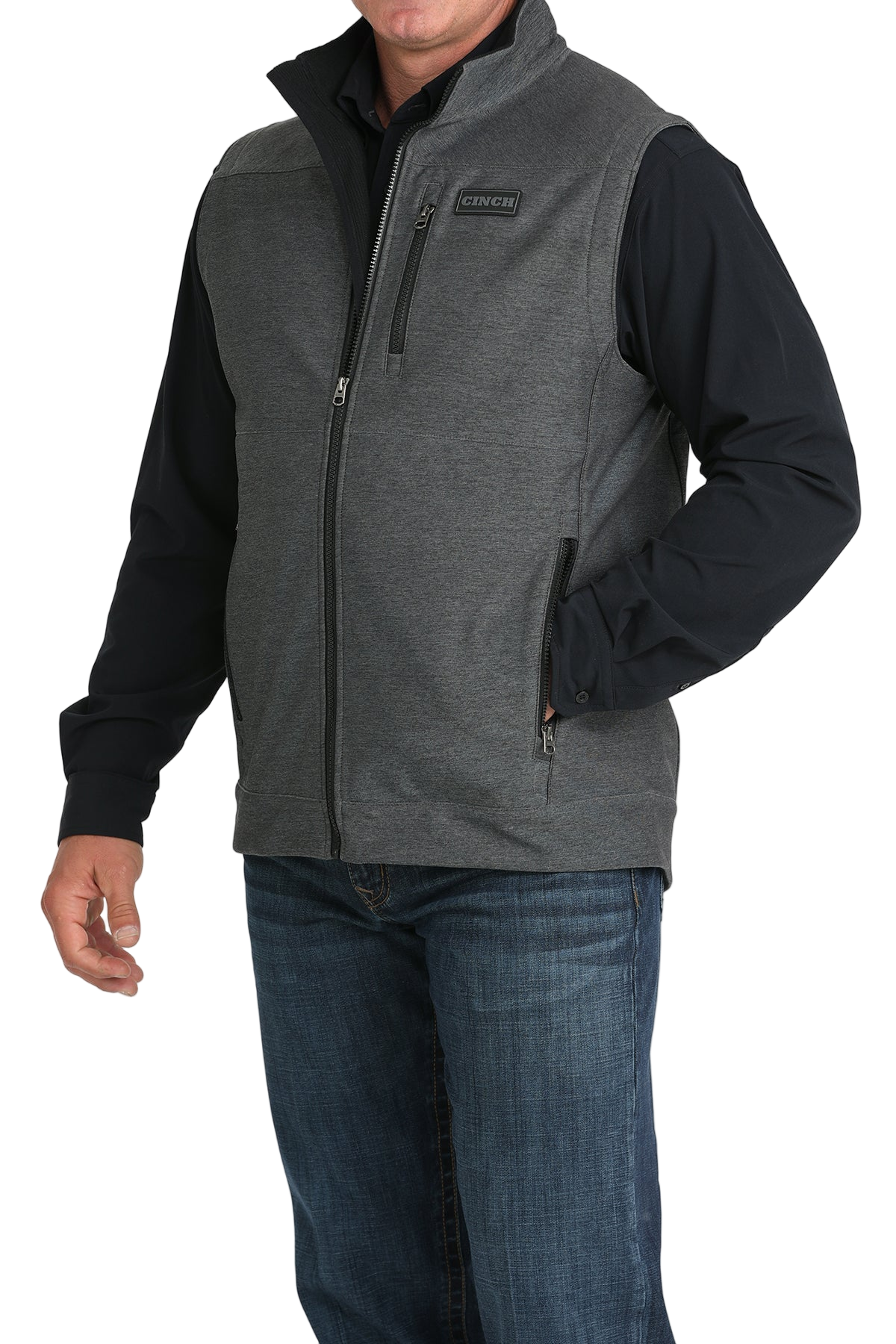 Man wearing a gray zip-up vest over a black long-sleeve shirt and jeans 