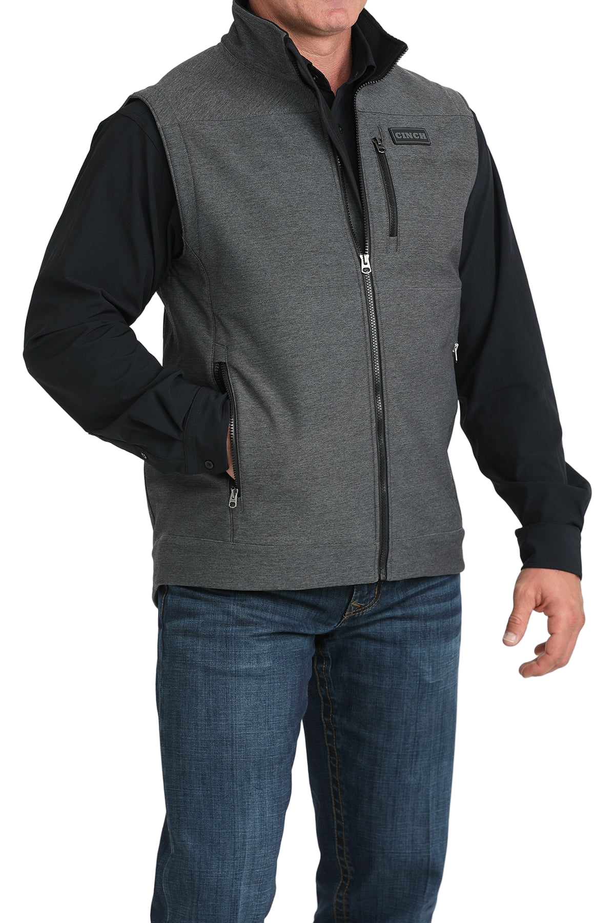 Man wearing a gray zip-up vest over a black long-sleeve shirt and jeans 