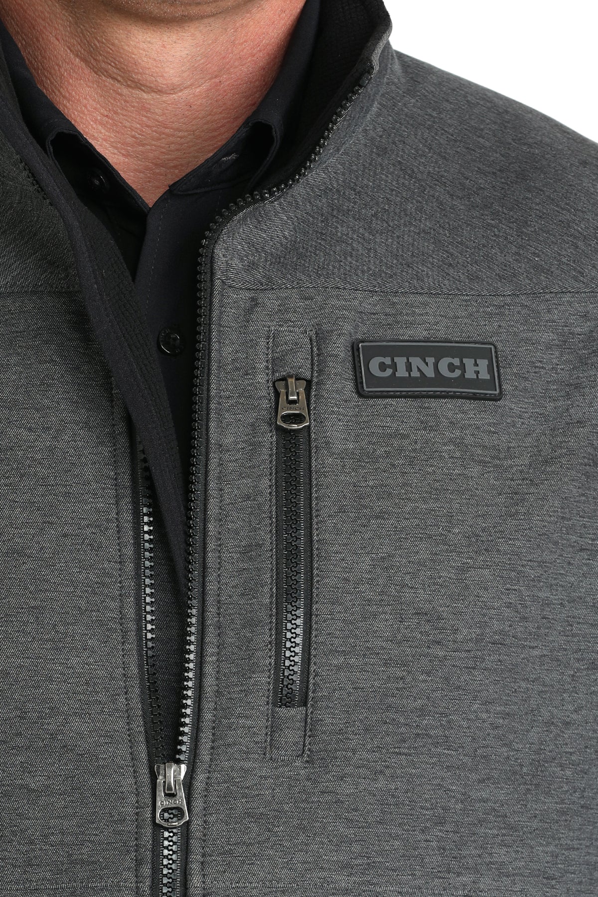 Close-up of a man wearing a dark gray vest with a cinch logo 