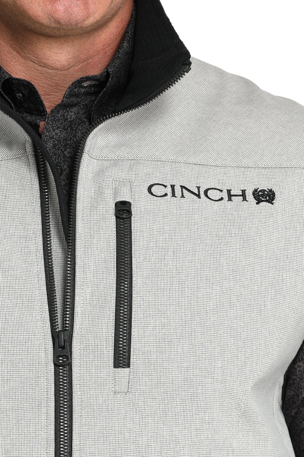 Close-up of a man wearing a gray vest with a cinch logo 
