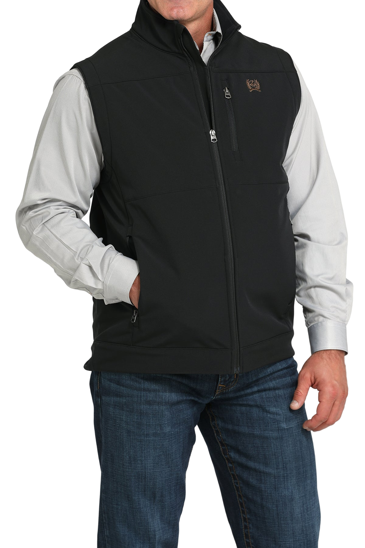 A man wearing a black zip-up vest over a light gray button-down shirt, paired with blue jeans