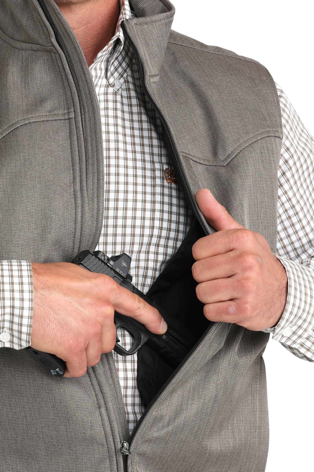 Close-up of a man wearing a grey vest over a checkered shirt, partially unzipping the vest to access an interior concealed carry pocket that holds a handgun