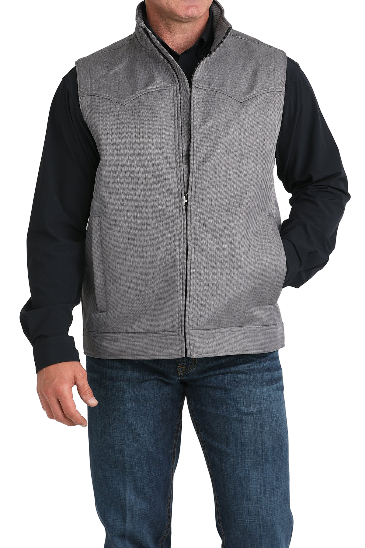 A man wears a light gray zip-front vest over a black long-sleeve shirt and blue jeans