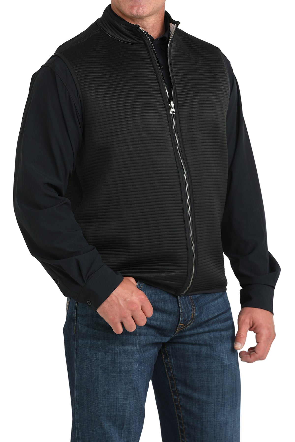 A man wears a black zip-front vest over a black long-sleeve shirt and blue jeans