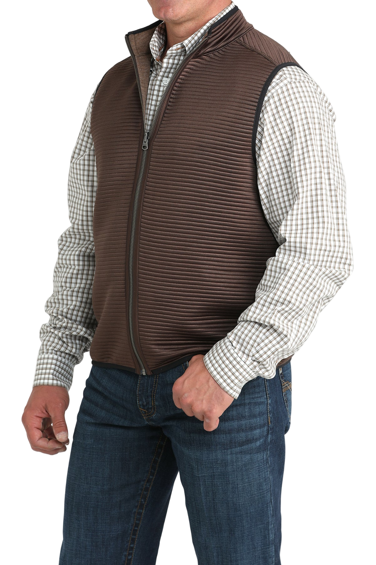 A man wearing a brown zip-up vest over a white and brown checkered button-down shirt, paired with blue jeans