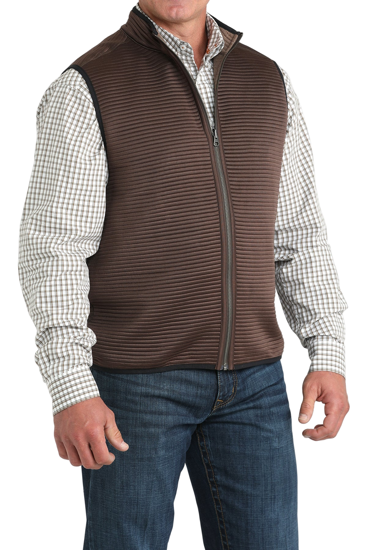 A man wearing a brown zip-up vest over a white and brown checkered button-down shirt, paired with blue jeans