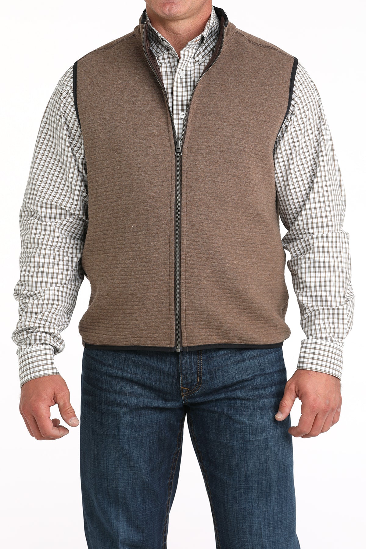 Man wearing a light brown vest with a checkered long sleeve undershirt and jeans 