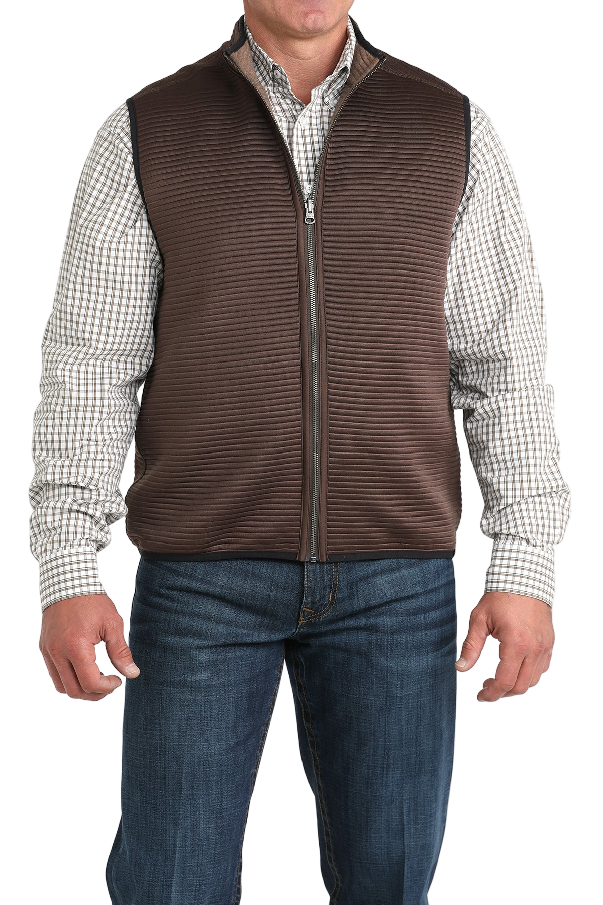 A man wearing a brown zip-up vest over a white and brown checkered button-down shirt, paired with blue jeans