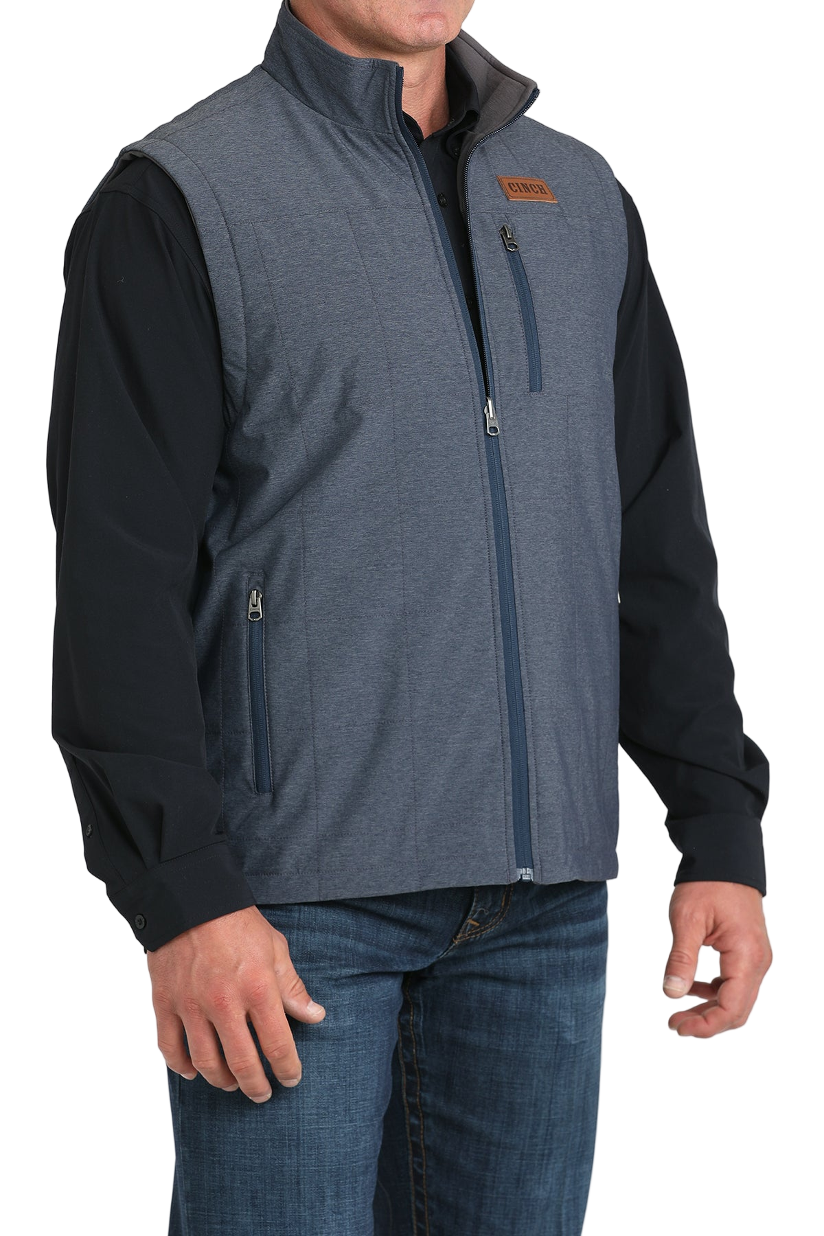 A man wearing a blue zip-up vest over a black shirt, paired with blue jeans