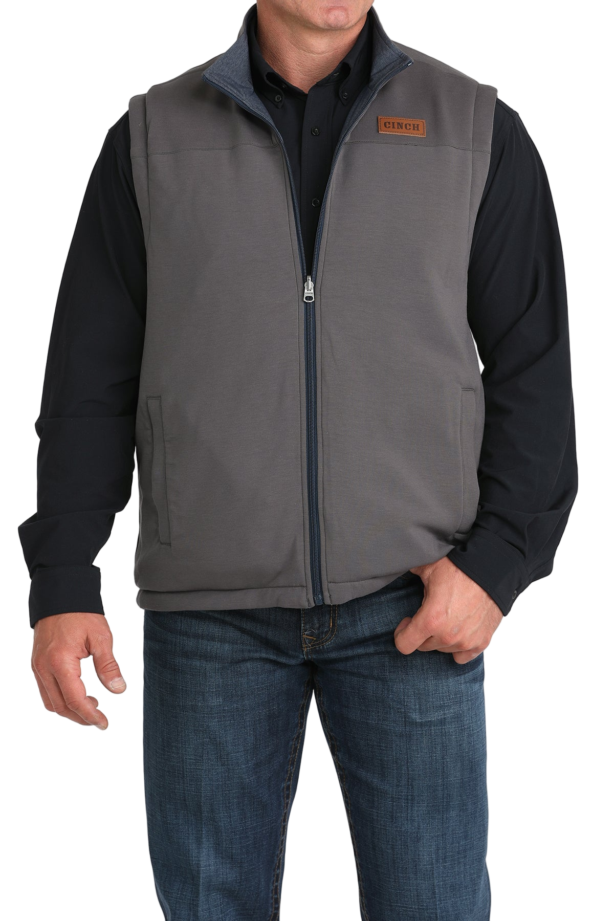 A man wearing a gray zip-up vest over a black shirt, paired with blue jeans