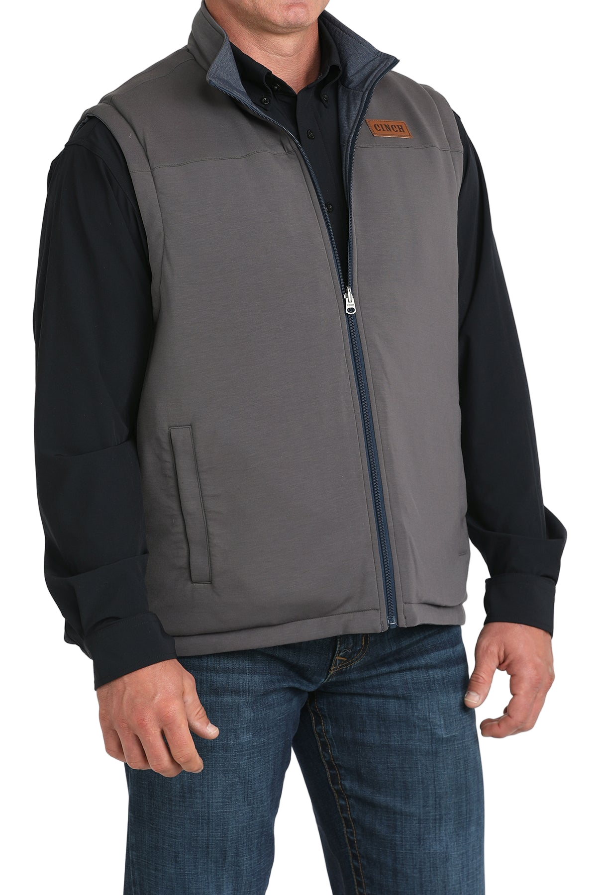 A man wearing a gray zip-up vest over a black shirt, paired with blue jeans