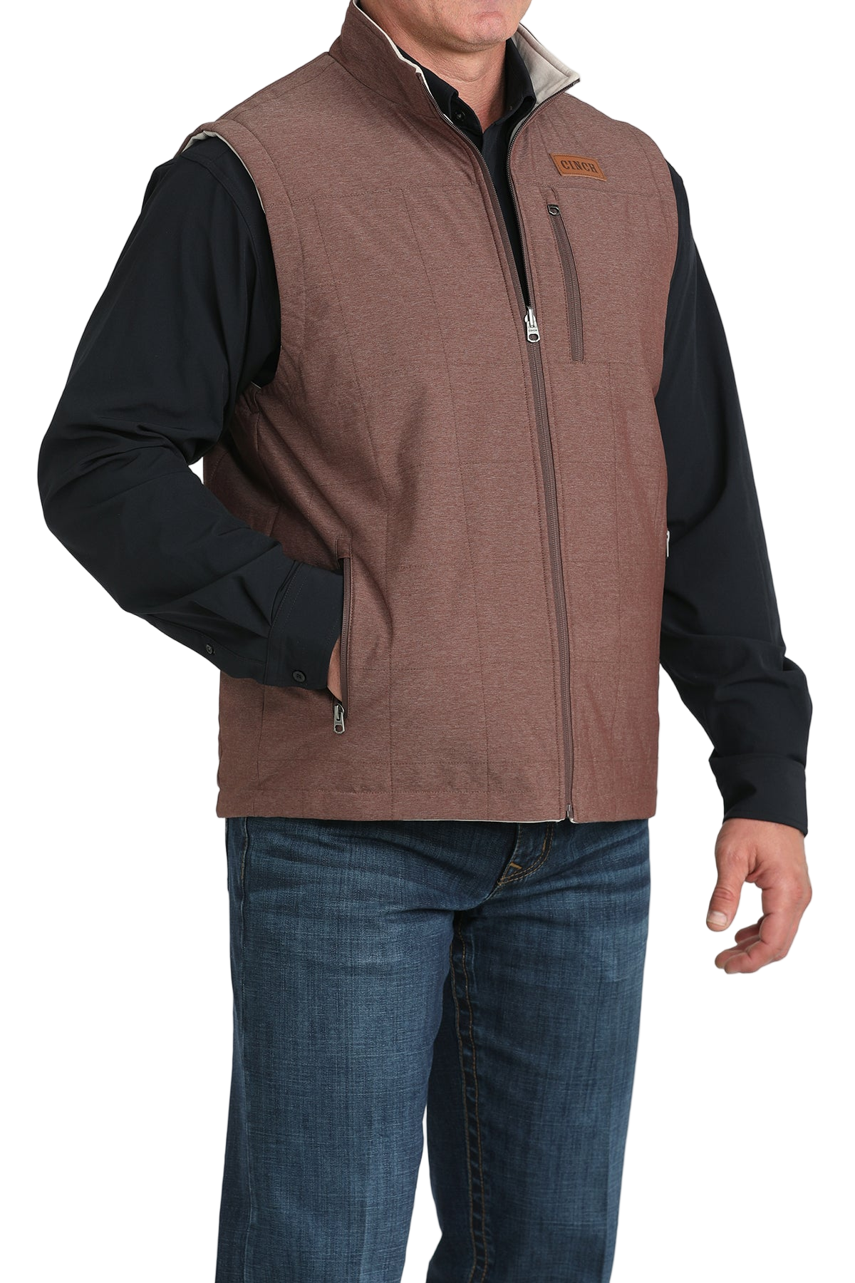 A man wears a maroon zip-front vest over a black long-sleeve shirt and blue jeans