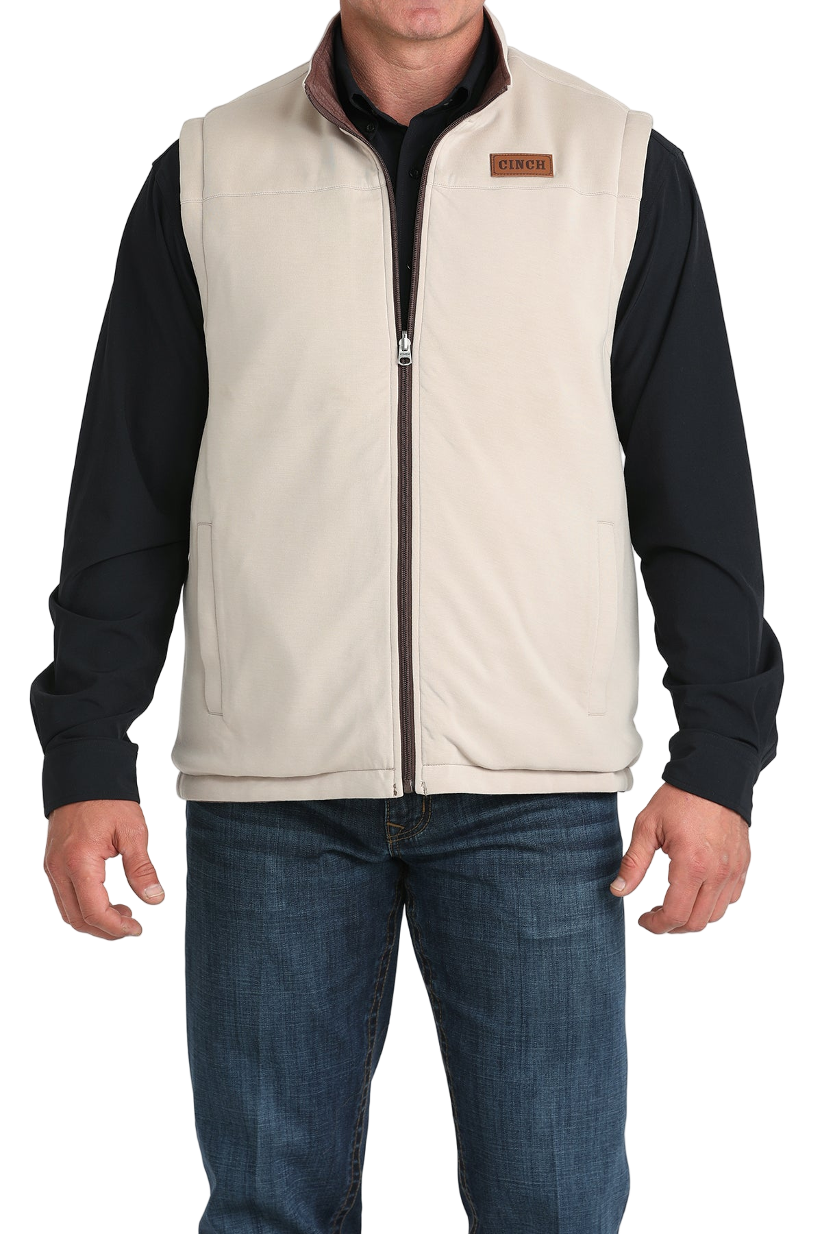 A man wears a white zip-front vest over a black long-sleeve shirt and blue jeans