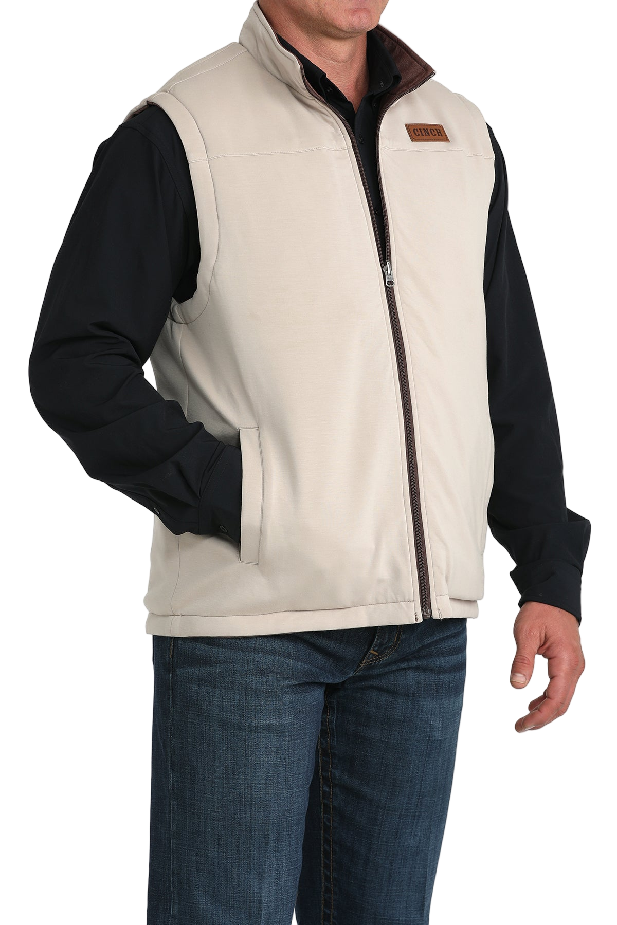 A man wears a white zip-front vest over a black long-sleeve shirt and blue jeans