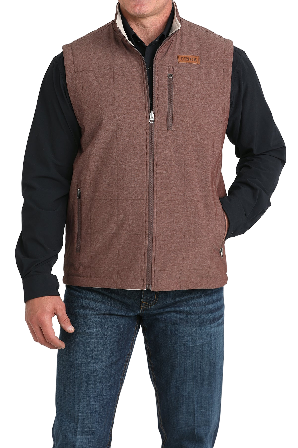 A man wears a maroon zip-front vest over a black long-sleeve shirt and blue jeans