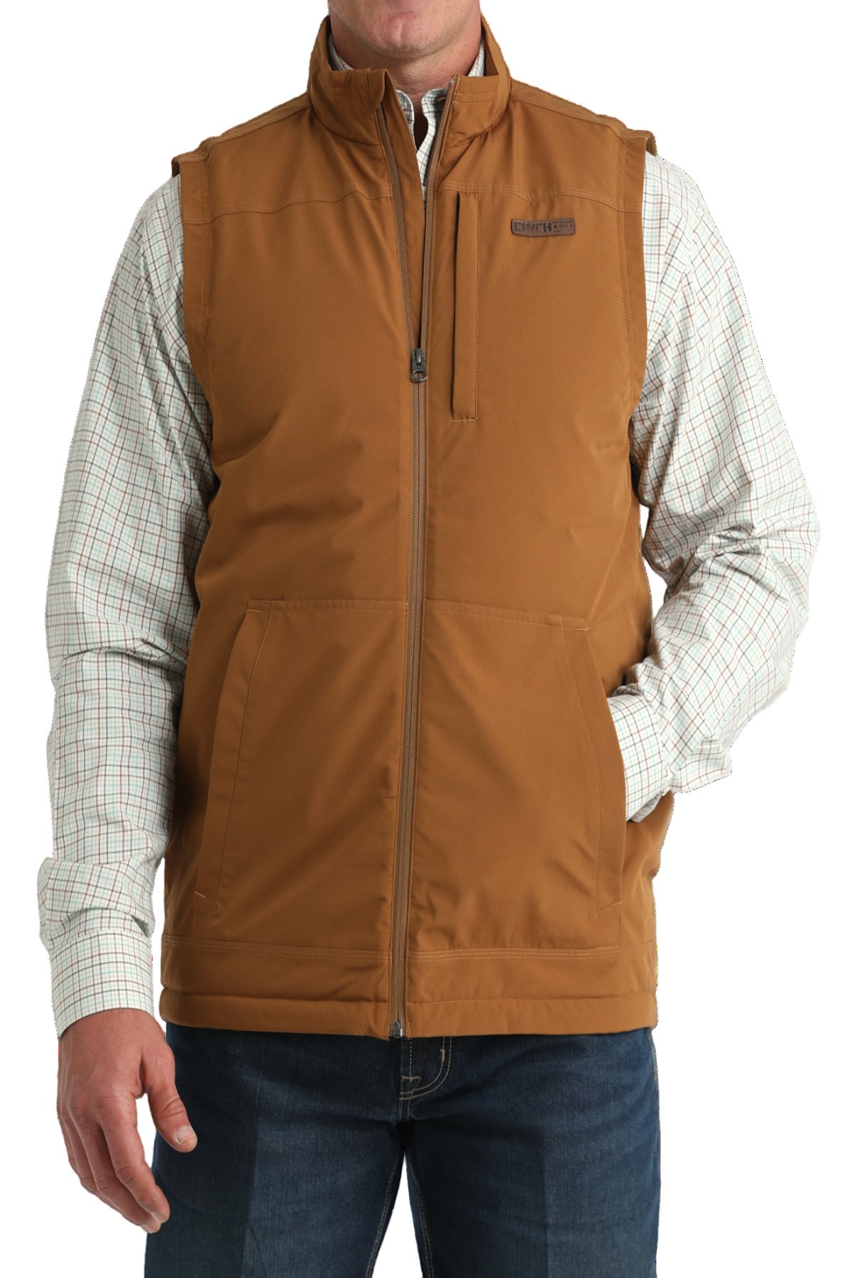 A man wearing a tan zip-up vest over a light plaid button-down shirt, paired with blue jeans