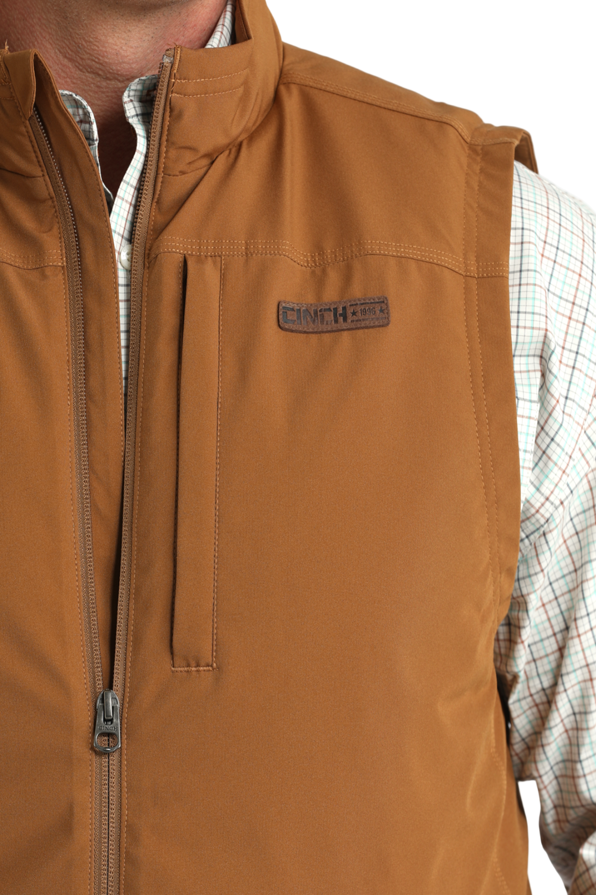 Close-up of a man wearing a tan zip-up vest over a light plaid button-down shirt