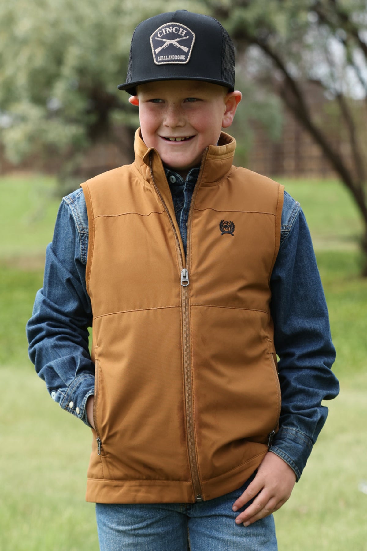 Child wearing a brown vest and blue jacket outdoors