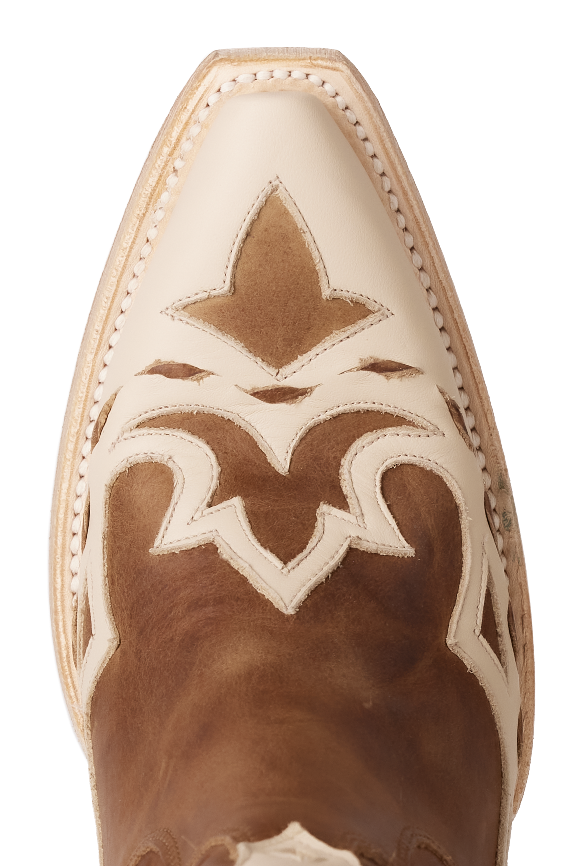 Close-up of a cowboy boot toe featuring a pointed cream-colored tip with intricate cream overlays stitched onto a rich brown leather base in a decorative western pattern