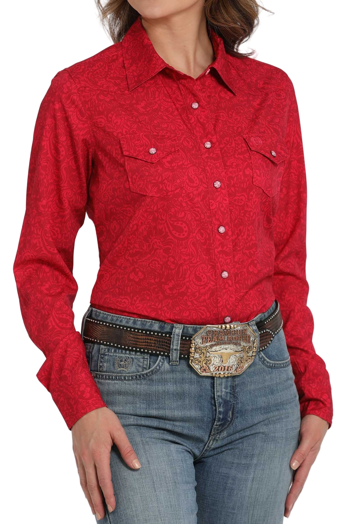 Woman wearing a red long-sleeve button-down shirt with an allover pattern, paired with light-wash jeans and a large silver western belt buckle