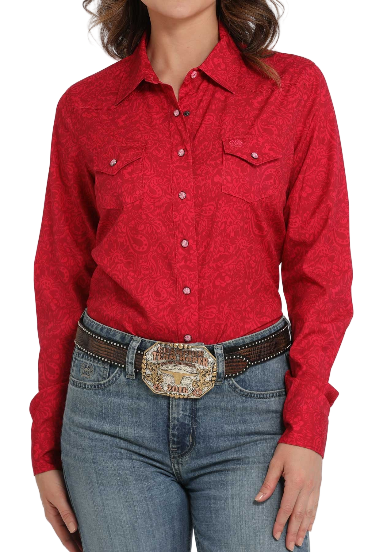 Woman wearing a red long-sleeve button-down shirt with an allover pattern, paired with light-wash jeans and a large silver western belt buckle